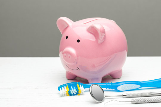 Pink piggy bank and dental tools with a toothbrush on a gray background. The concept of how to save on dental treatment