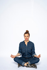 Beautyful woman in Studio in Modern Jeans outfit is sitting in a yoga seat