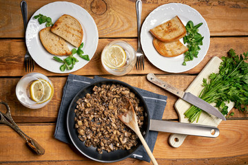 Stewed mushrooms in pan with toasts and parsley on wooden table