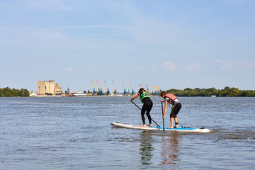 Teenagers - boy and a girl row on stand up paddleboard on the Danube river