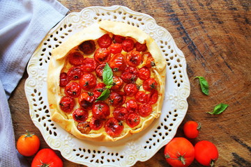 Delicious homemade rustic open pie or galette with tomato, cheese on wooden background. Top view
