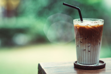 Horizontal shot of iced latte macchiato coffee in glass on wooden table outdoors. Latte macchiato is served in a tall glass and has distinctive layers of milk and espresso.