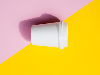 Flat lay small paper coffee cup isolated on a pink and yellow pop background. White espresso cup mockup with hard light and shadows