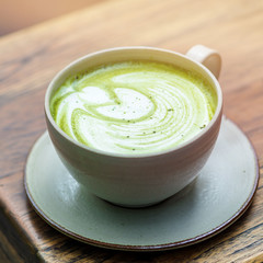 Close up shot of matcha latte in a white cup on wooden table. Matcha refers to finely-milled Japanese green tea. This type of latte is a creamy, delicious, antioxidant-filled drink.