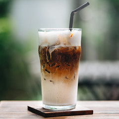 Close up shot of cold cappuccino in a glass with a straw on wooden table outdoors. Iced cappuccino...