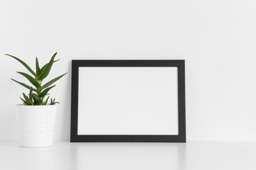 Black frame mockup with a aloe vera in a pot on a white table.Landscape orientation.