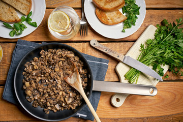 Stewed mushrooms in pan with toasts and parsley on wooden table