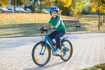 Happy kid boy, having fun in autumn park with a bicycle on beautiful fall day. Active child wearing helmet.