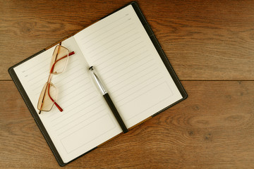 Business notebook composed with retro eyeglasses and pen on desk in office