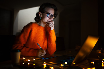 Portrait of smiling designer girl, working at graphic tablet on laptop. Wearing eyeglasses and...