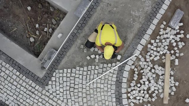 Granite Brick Paving by Caucasian Construction Industry Worker. Aerial View.