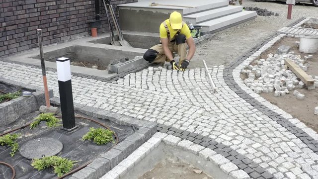 Professional Caucasian Worker Building Granite Paved Hardstanding Garden Path. Industrial Theme.