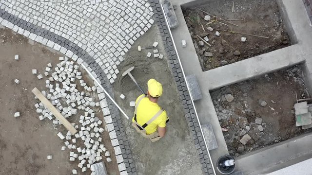 Bricks Driveway Building. Caucasian Construction Worker Finishing Granite Brick Road. Industrial Theme.