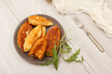 Plate with fried pies, fork on wooden boards