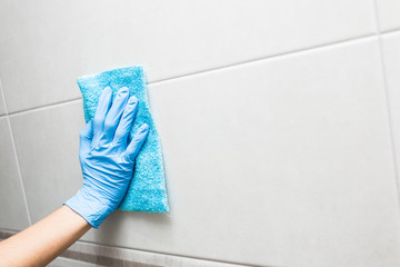 cleaning the toilet room, a hand in a blue glove washes a tile.