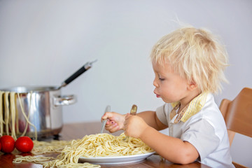 Little baby boy, toddler child, eating spaghetti for lunch and making a mess at home