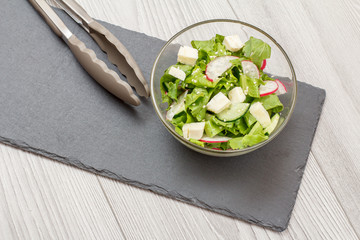 Fresh vegetable salad with cheese, cucumber and radish in glass bowl.