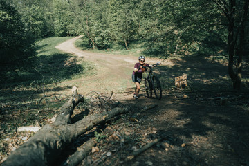 Photo of sportswoman in helmet raising bicycle to hill in forest