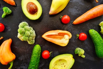 Composition with assorted fresh organic vegetables. Assorted fresh vegetables and fruits. Place for text. Cucumbers, tomatoes, pears, avocados, carrots, sweet peppers. Food on a dark table background.