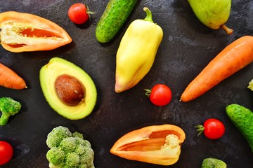 Composition with assorted fresh organic vegetables. Assorted fresh vegetables and fruits. Place for text. Cucumbers, tomatoes, pears, avocados, carrots, sweet peppers. Food on a dark table background.