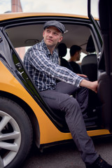 Image of young man in cap and plaid shirt looking to side sitting in back seat in yellow taxi