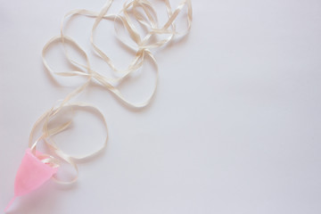 Menstrual cup with ribbon on white background. Close up, flatlay 