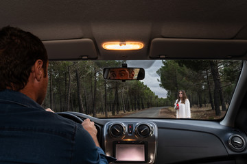 Scared man driving his car on a forest road and looking at a female ghost through the front...