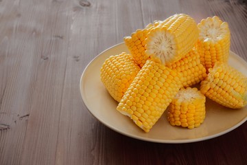 Sweet fresh corn on a beige ceramic plate on a wooden rustic table. Copy space for text.