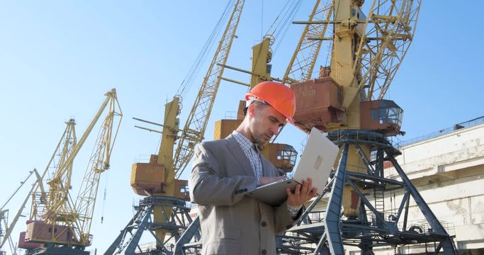 Young male worker of sea harbor in helmet, cargo manager in suit and halmet works outdoor , cranes and sea background	