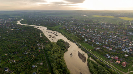 Aerial landscape of small town or village with rows of residential homes and green trees and big flloded river.