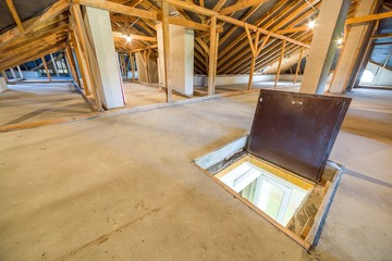 Attic of a building with wooden beams of a roof structure and a fire exit door in floor.