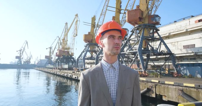 Young male worker of sea harbor in helmet, cargo manager in suit and halmet works outdoor , cranes and sea background	