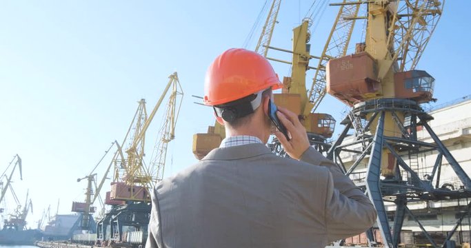Young male worker of sea harbor in helmet, cargo manager in suit and halmet works outdoor , cranes and sea background	