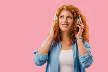 smiling curly girl listening music in headphones, Isolated On pink