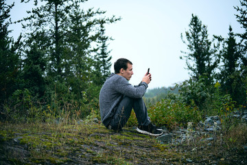 Young man in nature but isolated on his phone.