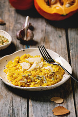 Traditional vegetarian pumpkin risotto italian dish in ceramic plate on old wooden kitchen table with ingredients above. Rustic style