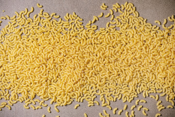 Raw uncooked italian pasta coquillettes in wooden bowl over brown texture background. Flat lay, space. Food background.