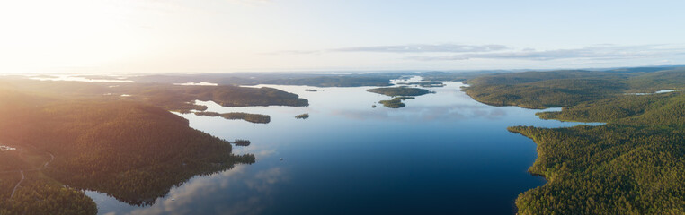 Aerial view of blue lake, reflections on water and green forests at sunset. Drone photography. ...