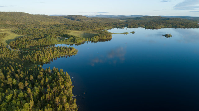 Aerial view of blue lake, reflections on water and green forests at sunset. Drone photography. 
