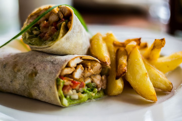 Tasty wraps with chicken, avocado, lettuce and french fries on a plate