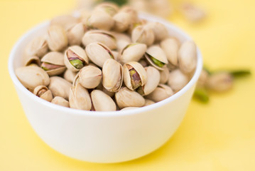 Salted pistachios in a bowl on a yellow background