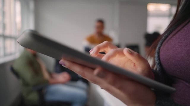 Close-up of a female entrepreneur in office using digital tablet standing in front of colleague having conversation in the office