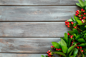 Green leaves and red berries frame on wooden background top view copyspace