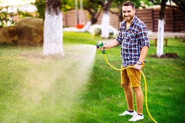 Professional gardener smiling working in garden, using hose and watering lawn and grass