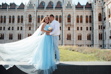 Obraz premium Young couple in love in Prague. Man in a white shirt. Pretty woman in a beautiful blue dress flying. Romantic fairytale couple near old building