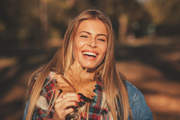Portrait of a beautiful blonde with a smile on face holding a leaf in hand in the park