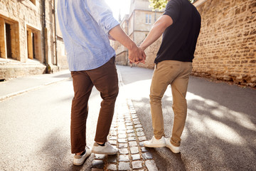 Rear View Of Male Gay Couple On Vacation Holding Hands Walking Along City Street
