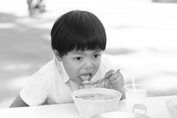An Asian boy eating rice congee with minced pork, boiled egg and vegetable in white ceramic bowl, black and white tone.