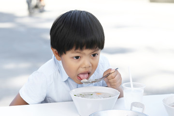 An Asian boy eating rice congee with minced pork, boiled egg and vegetable in white ceramic bowl.