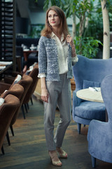 beautiful young smiling business brunette woman in elegant gray pantsuit and white shirt stands in a restaurant